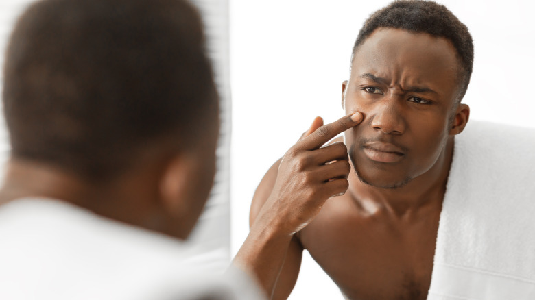 man looking at acne in the mirror