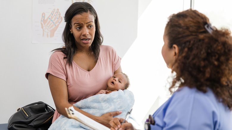 Woman holding newborn talking to doctor