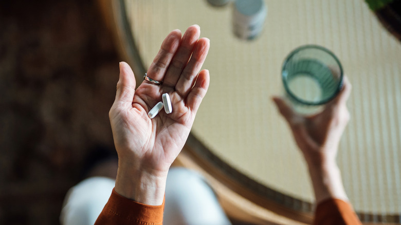 hands holding medications and a glass of water