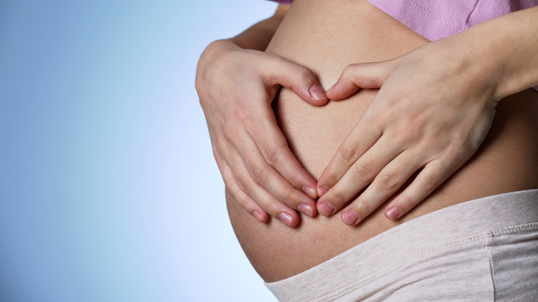 a woman making a heart with her hands on pregnant belly