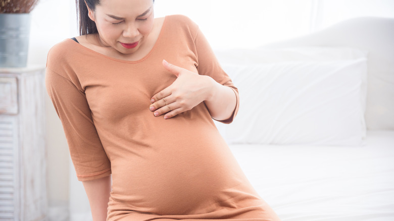 a pregnant woman holds her chest in discomfort from heartburn