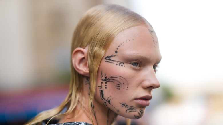 Side profile of a blonde model sporting face tattoos