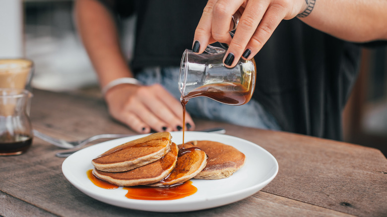Woman pouring maple syrup over pancakes