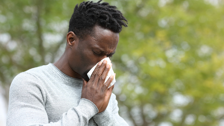 Man blowing nose outdoors