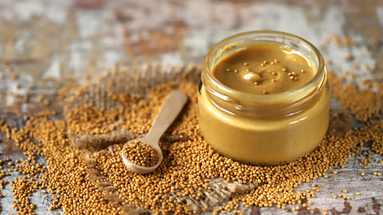 glass jar of mustard with mustard seeds on the side 