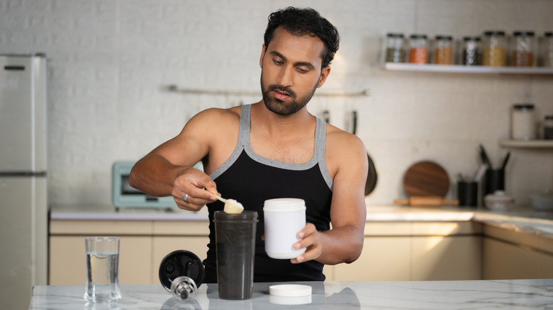focused man scooping powder into smoothie