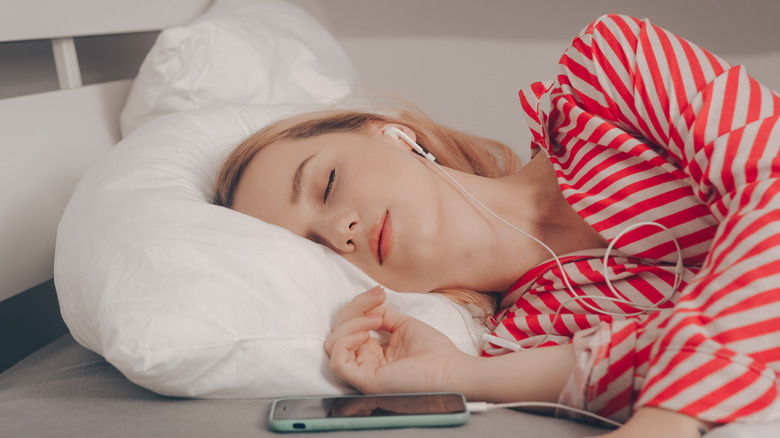 Woman sleeping with earbuds attached to phone