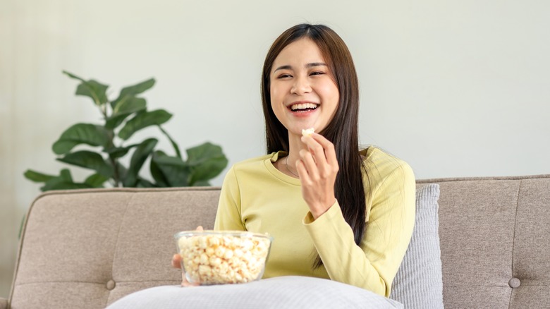 woman enjoying a bowl of popcorn while sitting on couch