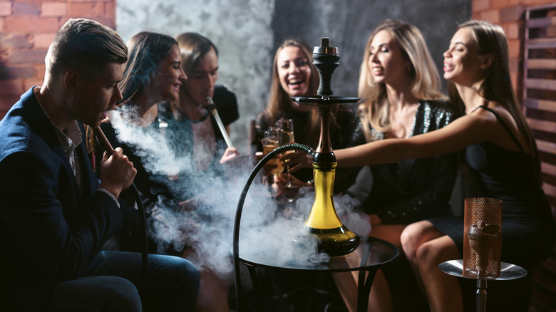 Group of smiling friends sitting around a table smoking hookah