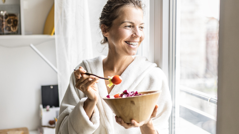 Smiling woman eating food by window