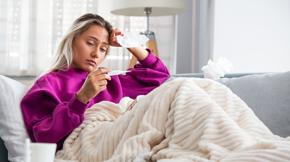 Sick woman in pink sweater checking the thermometer 