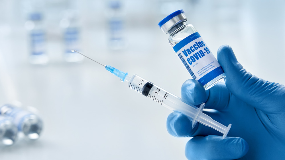 A gloved hand holding up a COVID-19 vaccine 