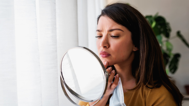 Woman looking at pimple in mirror