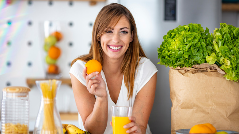 A woman eats and orange and drinks orange juice