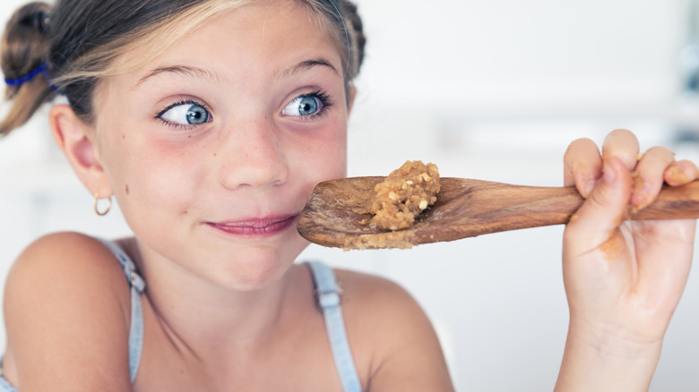 little girl eating cookie dough from a wooden spoon