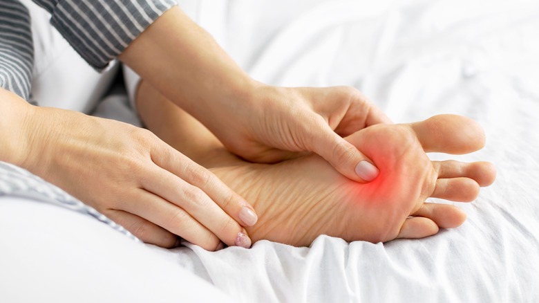 woman rubs sore red spot on foot 