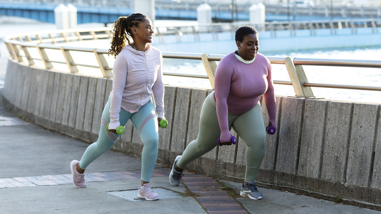 two women doing walking lunges on a boardwalk