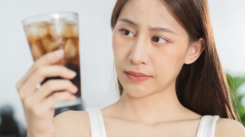 woman holding a soft drink in a glass staring curiously