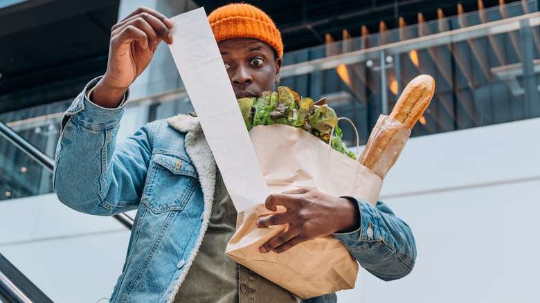 African American man carrying groceries looking at long receipt