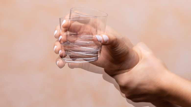 Closeup view on a shaking hand of a person holding a drinking glass