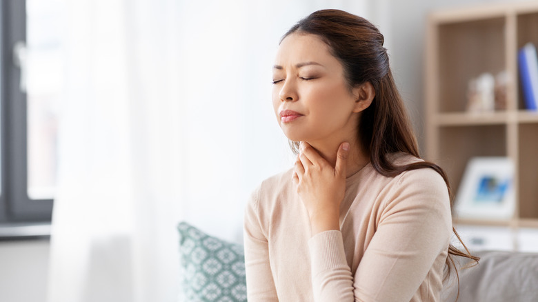 A woman holding her throat looking uncomfortable