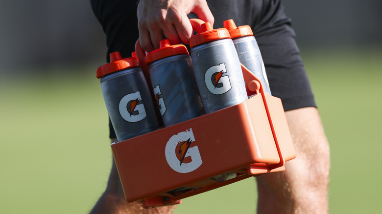 A hand carrying a carton of Gatorade bottles on a football field