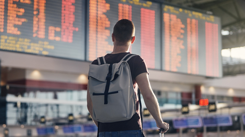 man in airport looking at screen with flights