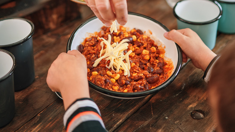 woman adding cheese to bean dish of chili