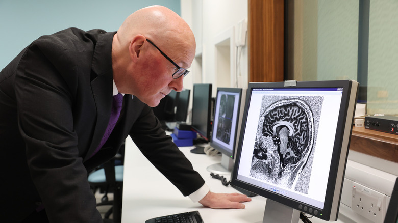 A blad man in a suit leaning over a desk and computer screen with image of a brain.
