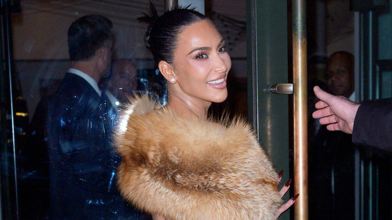 Kim Kardashian in a fur shawl, looking over her shoulder with a smile.
