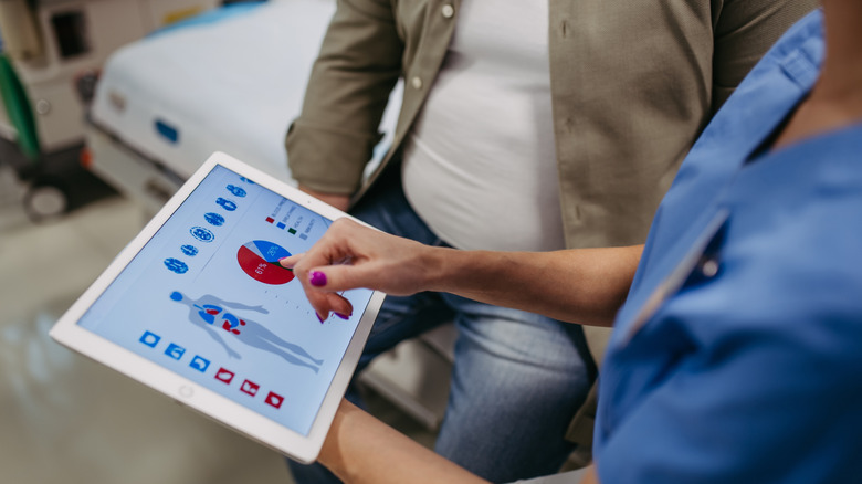 A person in scrubs pointing to a chart on an iPad screen to a man on a stretcher.