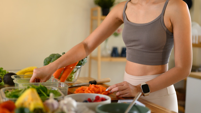 Woman in a crop top prepares a healthy meal consisting of a variety of vegetables