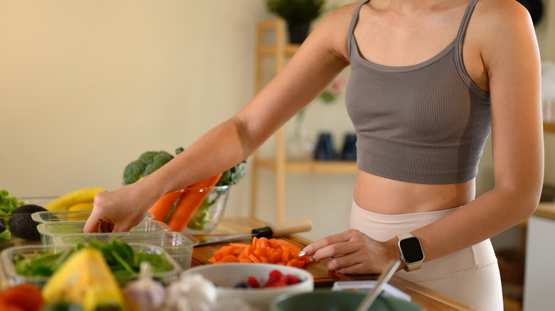 woman in a cropped tank top preparing a healthy meal made up of a variety of vegetables