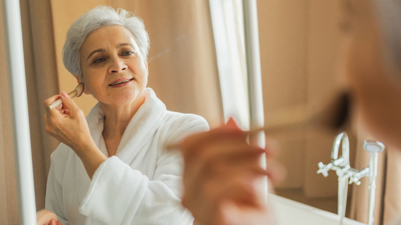 mature woman putting on face makeup in mirror