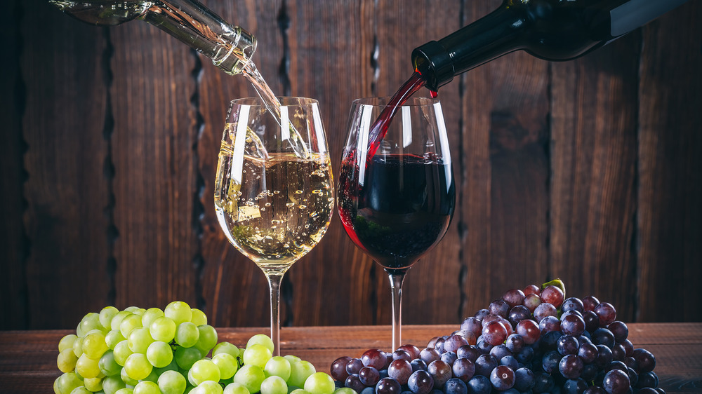 Two glasses of wine being poured next two red and white grapes