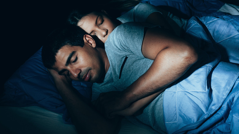 Couple sleeping together and holding one another in bed with light streaming in through window