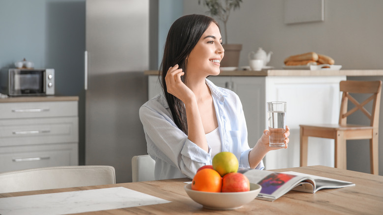 A woman holds a glass of water in her kitchen