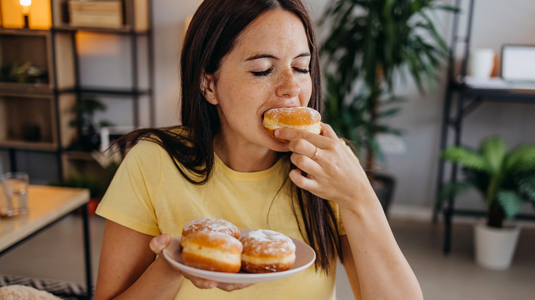 young woman eating plate of doughnuts