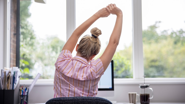 A woman stretches at her desk