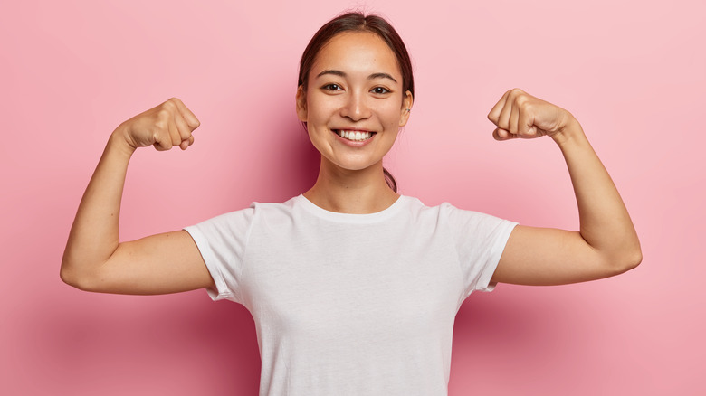 Woman in white tee smiling and raising her arms to show off muscles