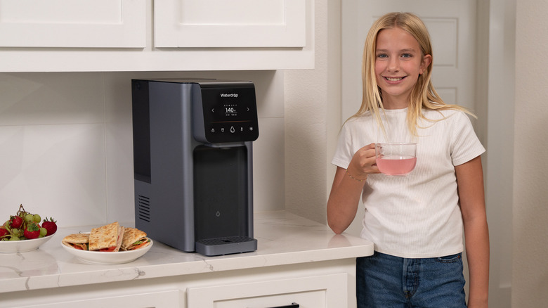 Young girl smiling holds cup of water from Waterdrop Filter dispenser.
