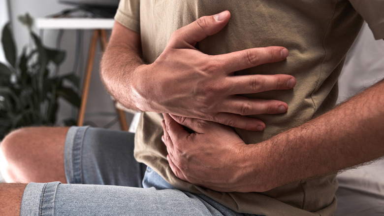 Close up on a man holding his side through a shirt.