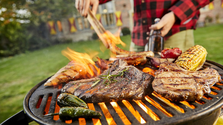 a man grills meat while holding a beer bottle