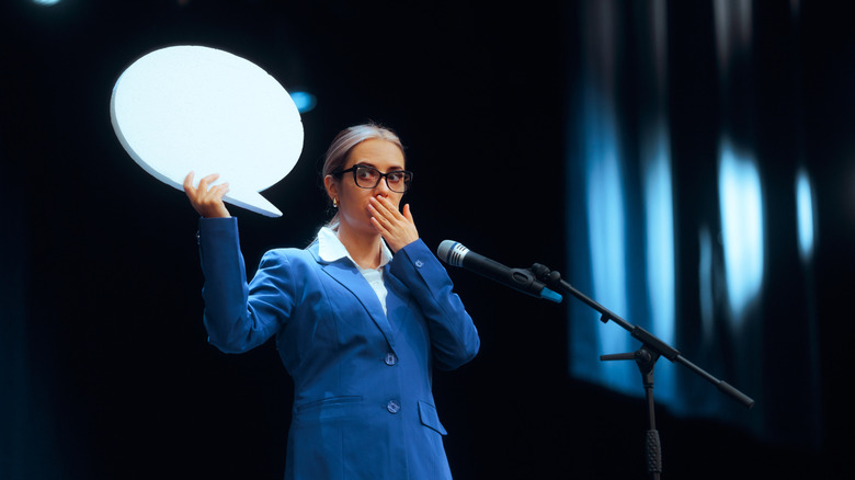 woman speaking on stage with hand over her mouth