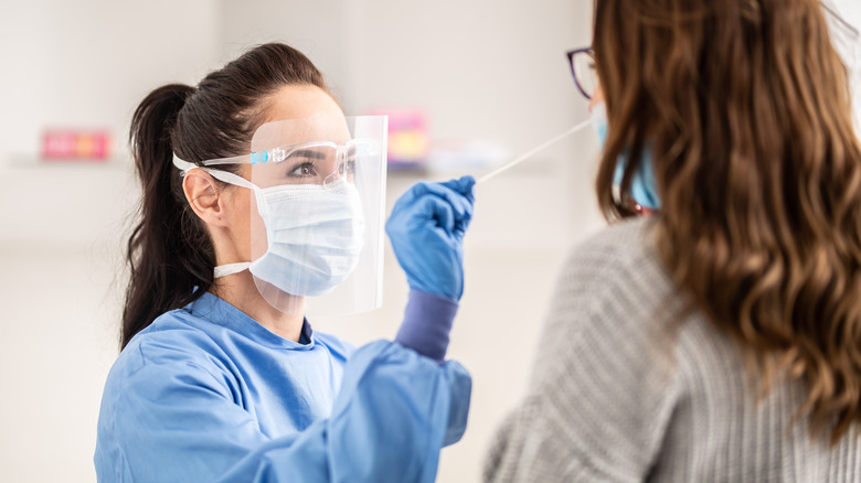 Medical staff worker wearing protective equipment takes sample from nose of a patient to antigen test for coronavirus.