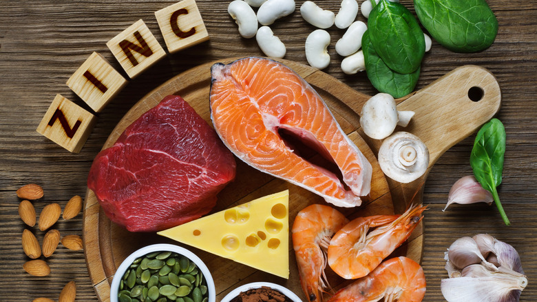 Foods high in zinc (salmon, shrimp, beef, yellow cheese, spinach, mushrooms, cocoa, pumpkin seeds, garlic, bean and almonds) alongside blocks spelling out the word ZINC 