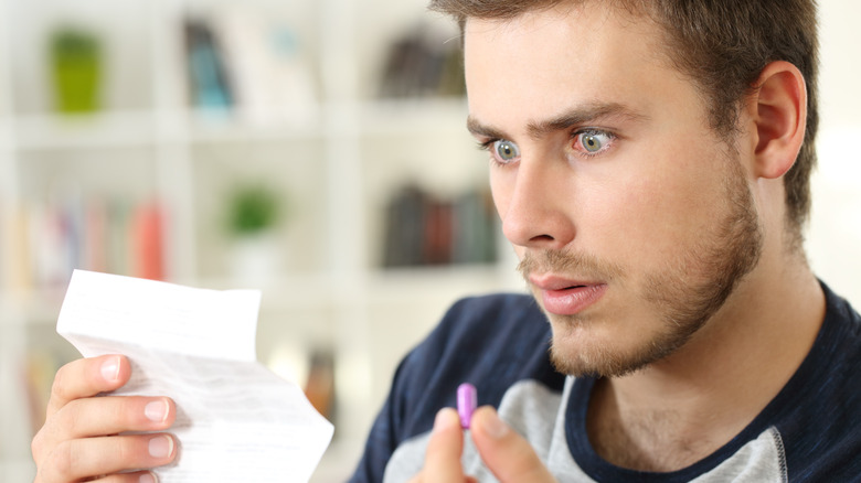 Surprised man reading a leaflet for a medication while holding a pill