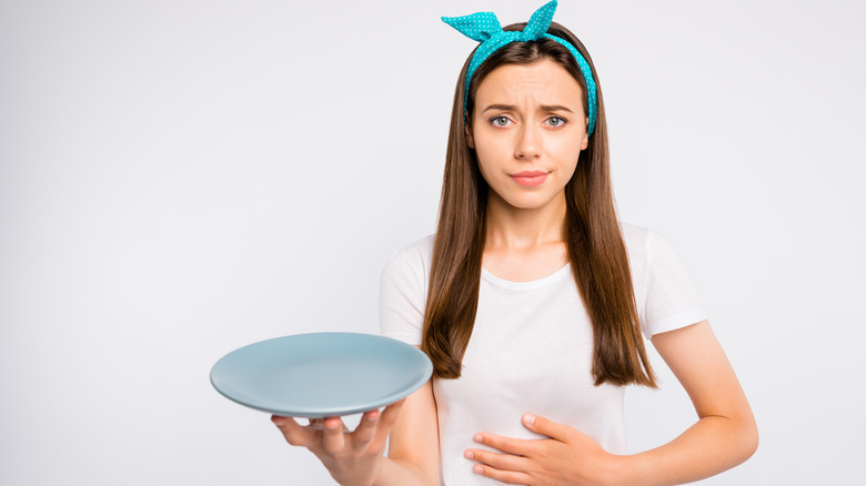 Young woman holding an empty plate and hungrily clutching her stomach