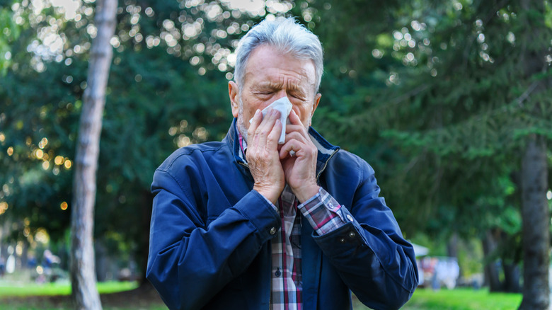 Senior man blowing his nose while on a walk