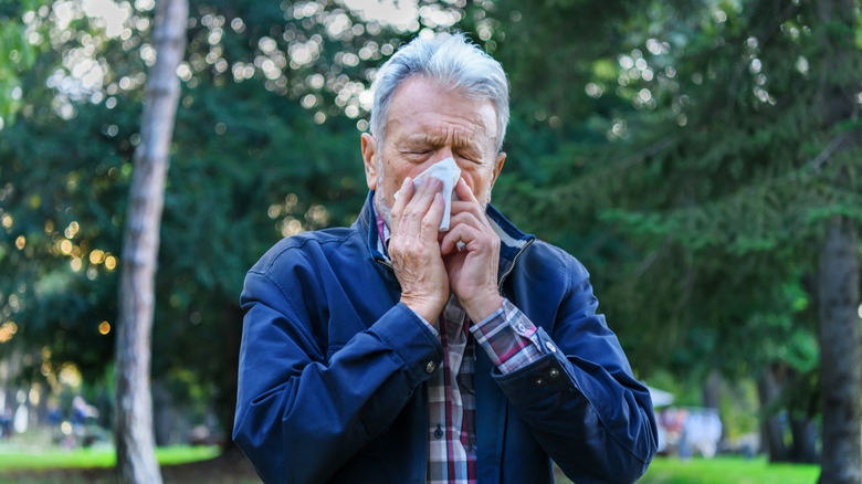 Senior man blowing his nose while on a walk